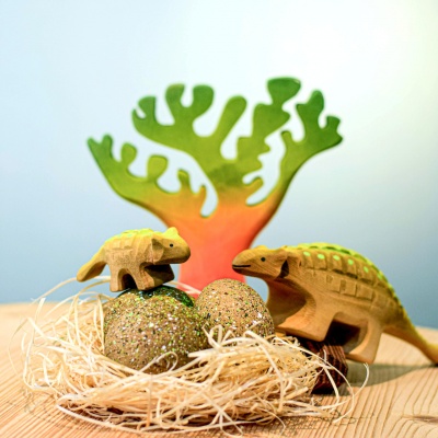 Wooden Ankylosaurus dinosaurs with three eggs in a straw nest, surrounded by wooden trees.