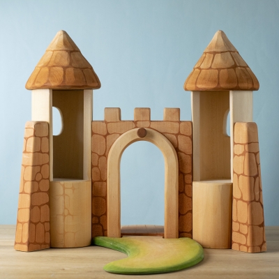 Rear view of open wooden castle showing tower interiors and grassy path.