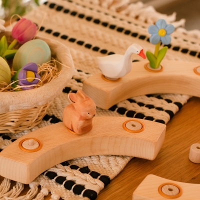Wooden celebration ring pieces holding a bunny, goose, and blue forget-me-not near an egg basket