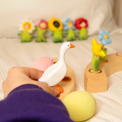 Woven basket filled with pastel Easter eggs, a wooden hen, chicks, and a white goose figure