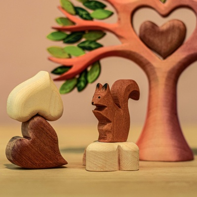 A decorative wooden tree with a heart at its center, surrounded by playful wooden squirrels and additional hearts. The tree and decorations are displayed on a table.