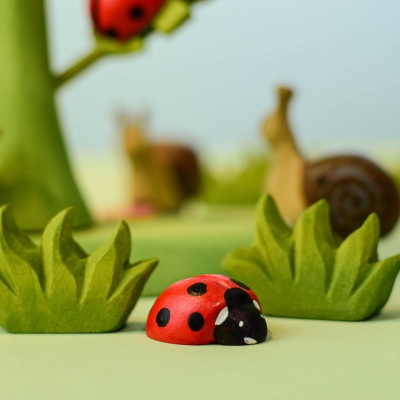 Handcrafted wooden ladybug toy on a grassy field with snails and trees by Bumbu Toys