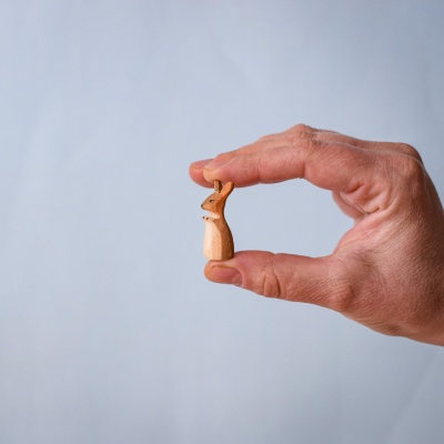 Tiny wooden joey toy held between two fingers for scale