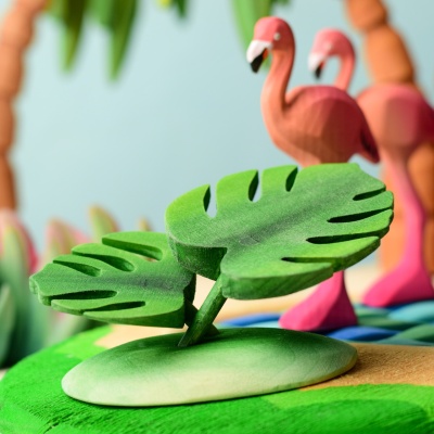 Group of Monstera wooden toys in a vibrant play scene with flamingos.