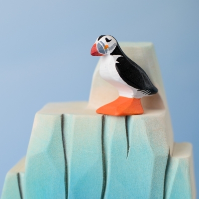 Small wooden puffin figure perched on the edge of a blue wooden iceberg toy.