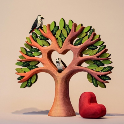 A wooden tree with a heart-shaped cutout in the center, perched on a red base. Two small birds sit on top of the tree.