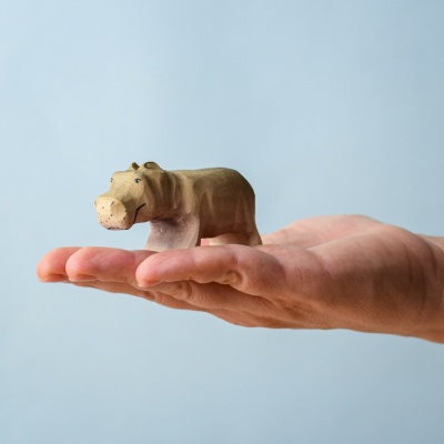 Wooden baby hippo toy held in hand for size reference.