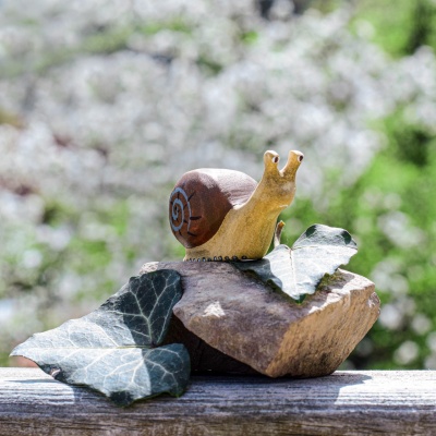 Wooden snail figurine on a rock with leaves