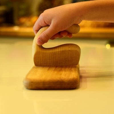 Close-up of a child using the wooden chopper on a cutting board