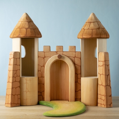 Rear view of wooden castle showing tower interiors and grassy path with closed gate..