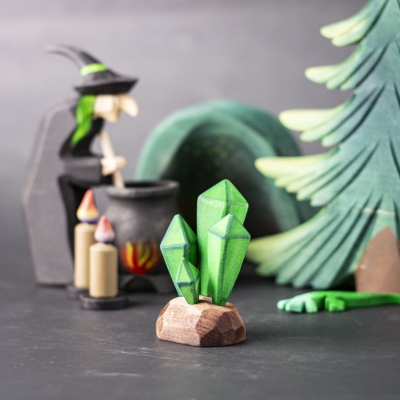 Green crystal toy placed in a fantasy scene with a witch, trees, and cauldron.