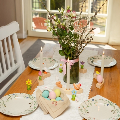 Easter table setting with candles in a wooden ring decorated with a daffodil, goose, and hen next to a basket of eggs