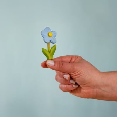 Hand holding a small blue wooden toy forget-me-not showing its size
