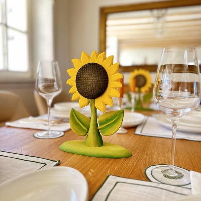 A wooden sunflower decor piece on a dining table set with white plates, glasses, and green napkins, creating an elegant setting.
