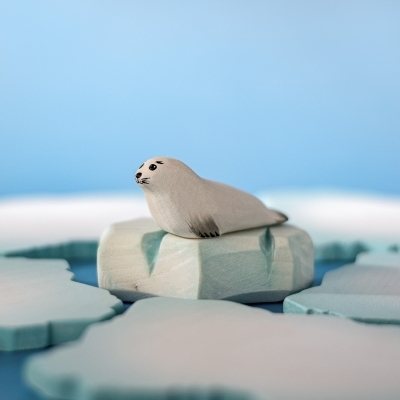 White wooden baby seal figure resting on a blue wooden ice block toy.