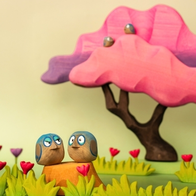 Miniature wooden birds perched on a pink wooden tree toy in a fantasy play scene