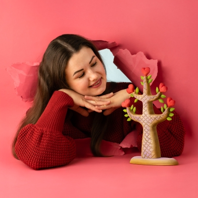 Lifestyle shot of a woman smiling next to the wooden Heartwood Tree, framed by a pink creative background.