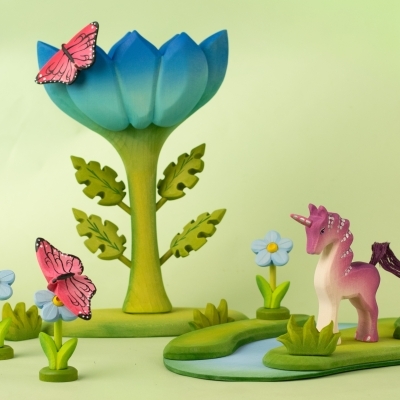 Large wooden blue flower toy with butterflies and a pink unicorn figure by a play river