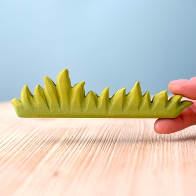Child holding Large Grass wooden toy next to other BumbuToys figurines, creating a miniature meadow scene.