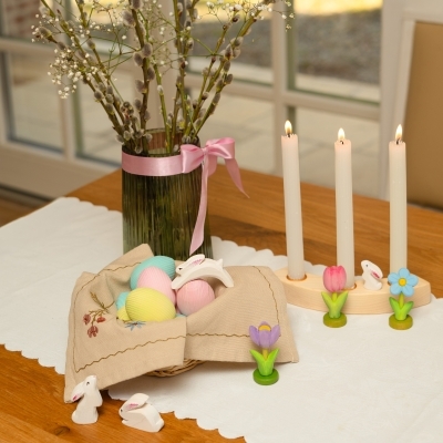 Spring table decor featuring a wooden ring with lit candles, a bunny, and a pink tulip next to a basket of eggs