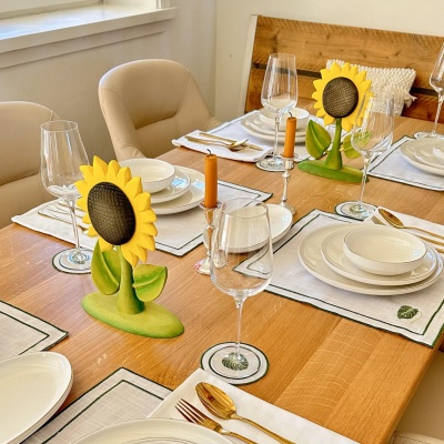 Two wooden sunflower toys as centerpiece decorations on a dining table set for a meal with white dinnerware and wine glasses.