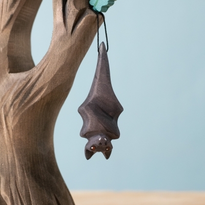 Handmade Huggy Bat wooden toy hanging upside down from a tree.