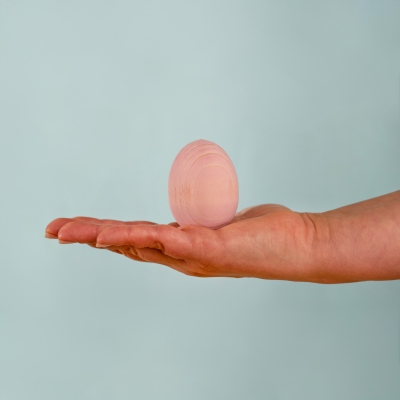 Hand holding a smooth pastel pink wooden toy egg showing its perfect size