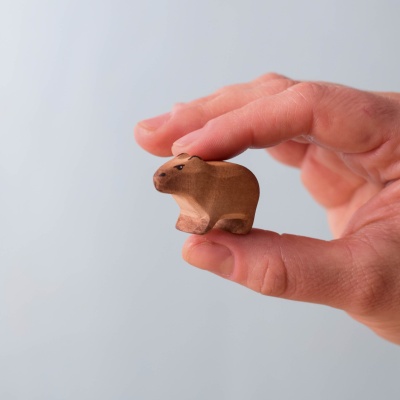 Small wooden baby capybara held between fingers, showing its size.