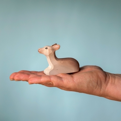 Small wooden Sitting Reindeer Calf toy held in an adult palm to show its smooth texture and compact size.
