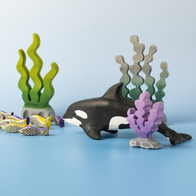 Adult Orca swimming among purple coral and seaweed in a play setup