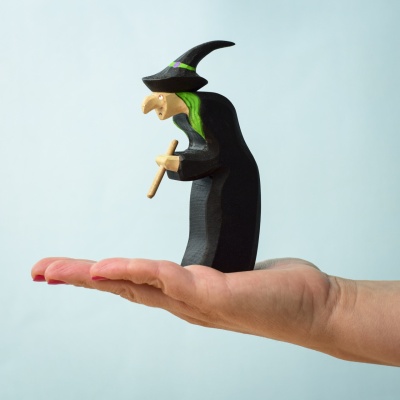 Hand holding a small handcrafted wooden brewing witch figurine.