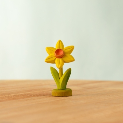 Wooden bunnies sitting near a yellow daffodil supported by a green toy base