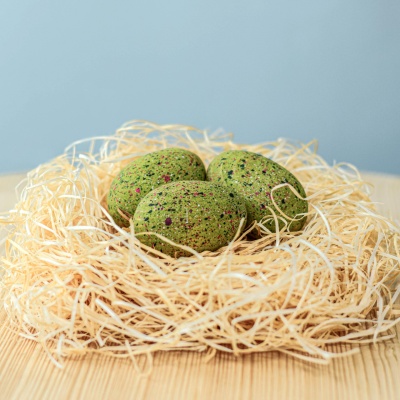 A set of three handcrafted wooden T-Rex eggs nestled on a bed of straw or leaves.
