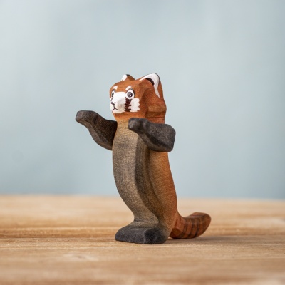 Upright red panda with expressive arms raised beside bamboo
