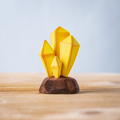 Yellow wooden crystal cluster on a dark brown wooden base, photographed on a wooden surface.
