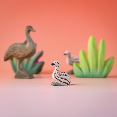 Sitting emu chick in a playful nature setup with emu family