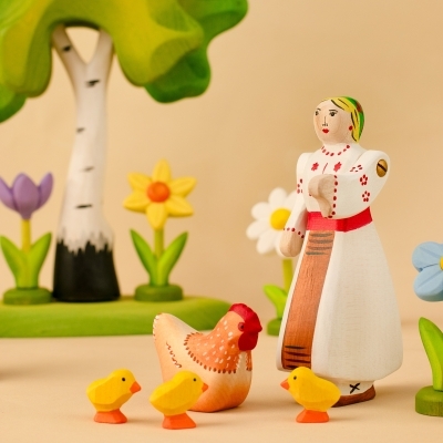 Traditional wooden Romanian girl figure with a hen, tiny chicks, birch trees, and a yellow spring daffodil toy