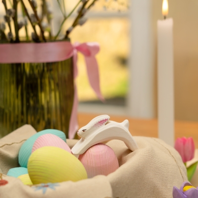 White wooden leaping bunny toy placed on pastel Easter eggs in a cloth lined woven basket