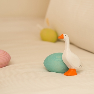 Close up of a wooden white goose toy and tiny wooden ducklings near a nest in a spring play scene