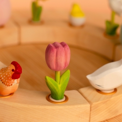 Pink wooden toy tulip placed in a wooden celebration ring next to a painted wooden hen