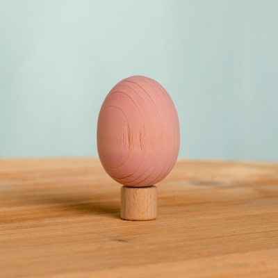 Single pastel pink wooden toy egg standing upright on a wooden table
