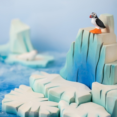 Close-up of a wooden puffin toy standing on the peak of a wooden glacier backdrop.