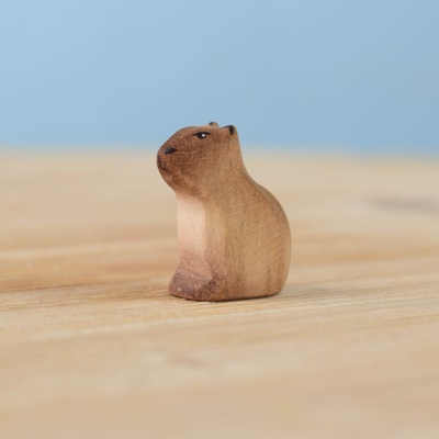 Handmade wooden baby capybara sitting on a wooden surface.