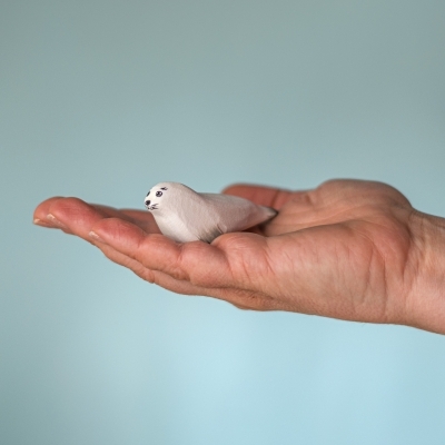 Small wooden seal pup toy held in an adult hand to show the 6.5cm size for toddlers.