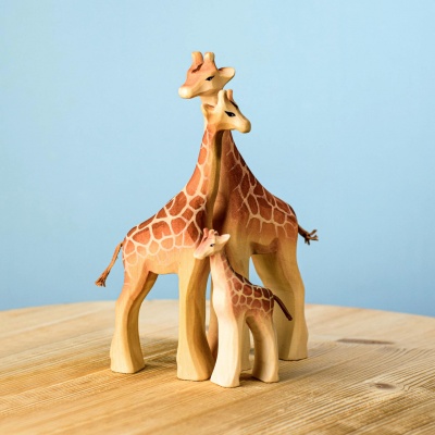 Wooden giraffe calf toy beside a larger giraffe on a wooden surface. Alt Text for Image 5: Wooden giraffe family including calf, female, and male giraffes.