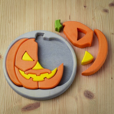 Round Halloween puzzle with pieces partially disassembled, showcasing the jack-o'-lantern face on a grey base.