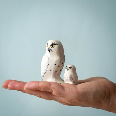 Close-up of a Snowy Owl figurine with a chick resting in a hand.
