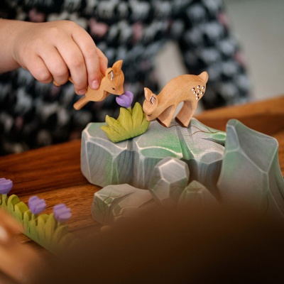 A child using the wooden fawn toy to create a story alongside other animal figurines.