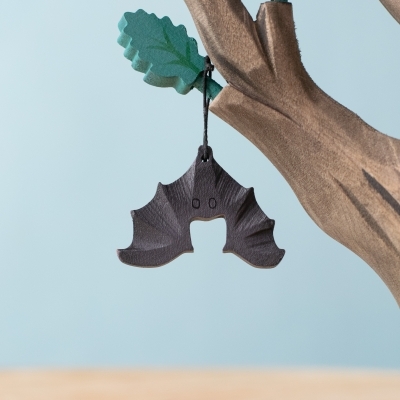 Handmade Nappy Bat wooden toy hanging upside down from tree branch.