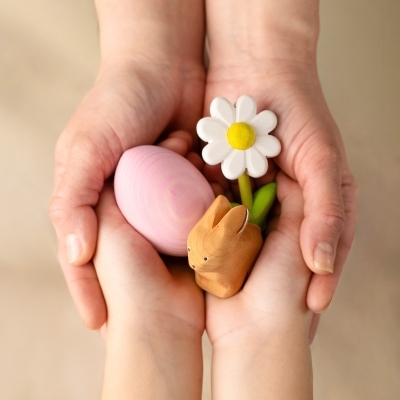 Adult and child hands holding a wooden daisy a pink wooden egg and a wooden bunny